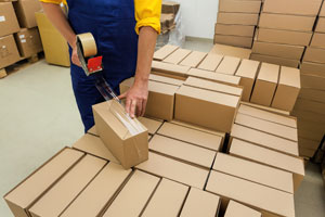 Warehouse worker taping a small box on top of more boxes on a loaded pallet.